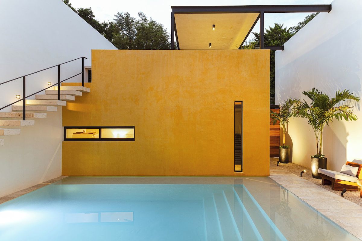 Area piscina interna moderna con pavimento in vetro trasparente, una scala e una zona relax con piante.