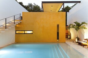 Un espace piscine intérieur moderne doté d’un sol en verre transparent, d’un escalier et d’un coin salon agrémenté de plantes.