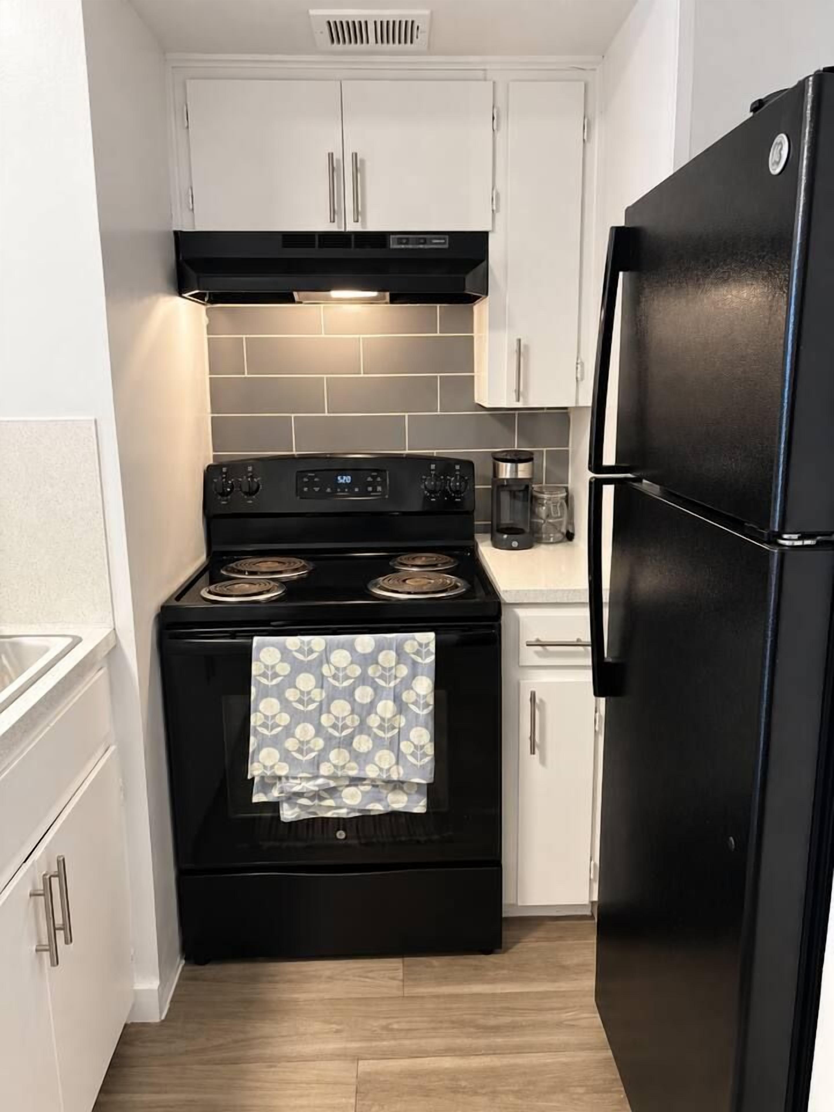 A compact kitchen with white cabinetry, a black stove, and a black refrigerator.