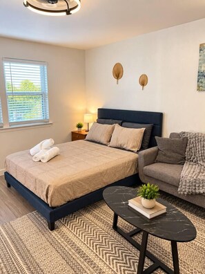 A bedroom with a bed, a sofa, a small table, and a wall-mounted lamp. - Bright Studio in Allandale | Near The Domain (Austin)