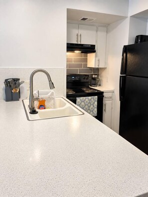 A kitchen with a white countertop, stainless steel sink, and a black refrigerator.