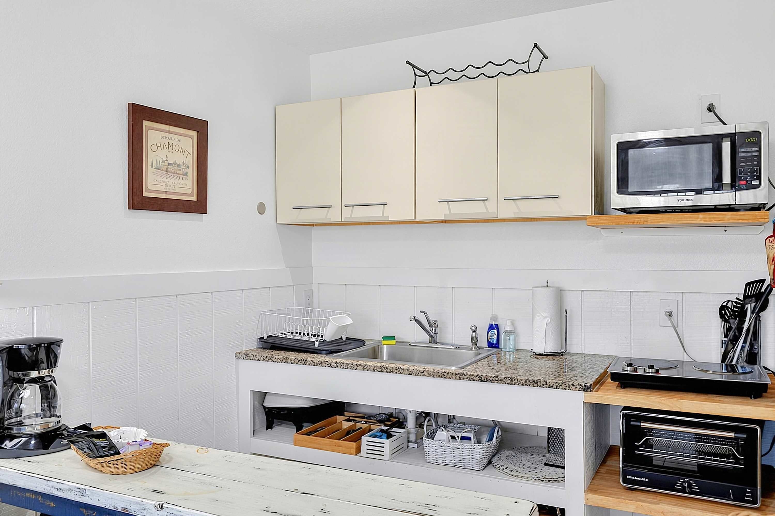 A kitchen with white cabinets, a microwave, a coffee maker, and a sink.