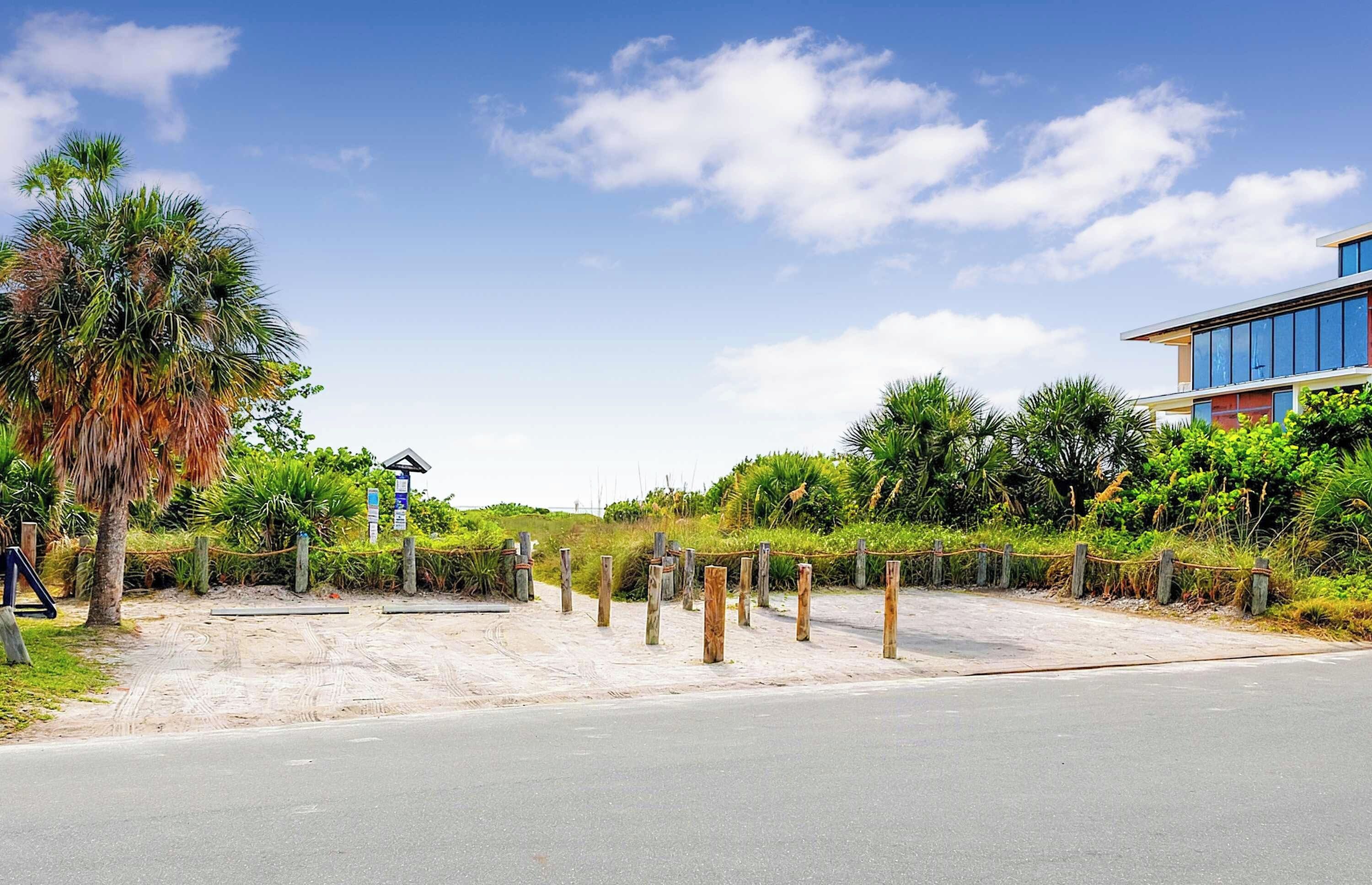 A beachfront property with a paved walkway, palm trees, and a modern building with large windows.