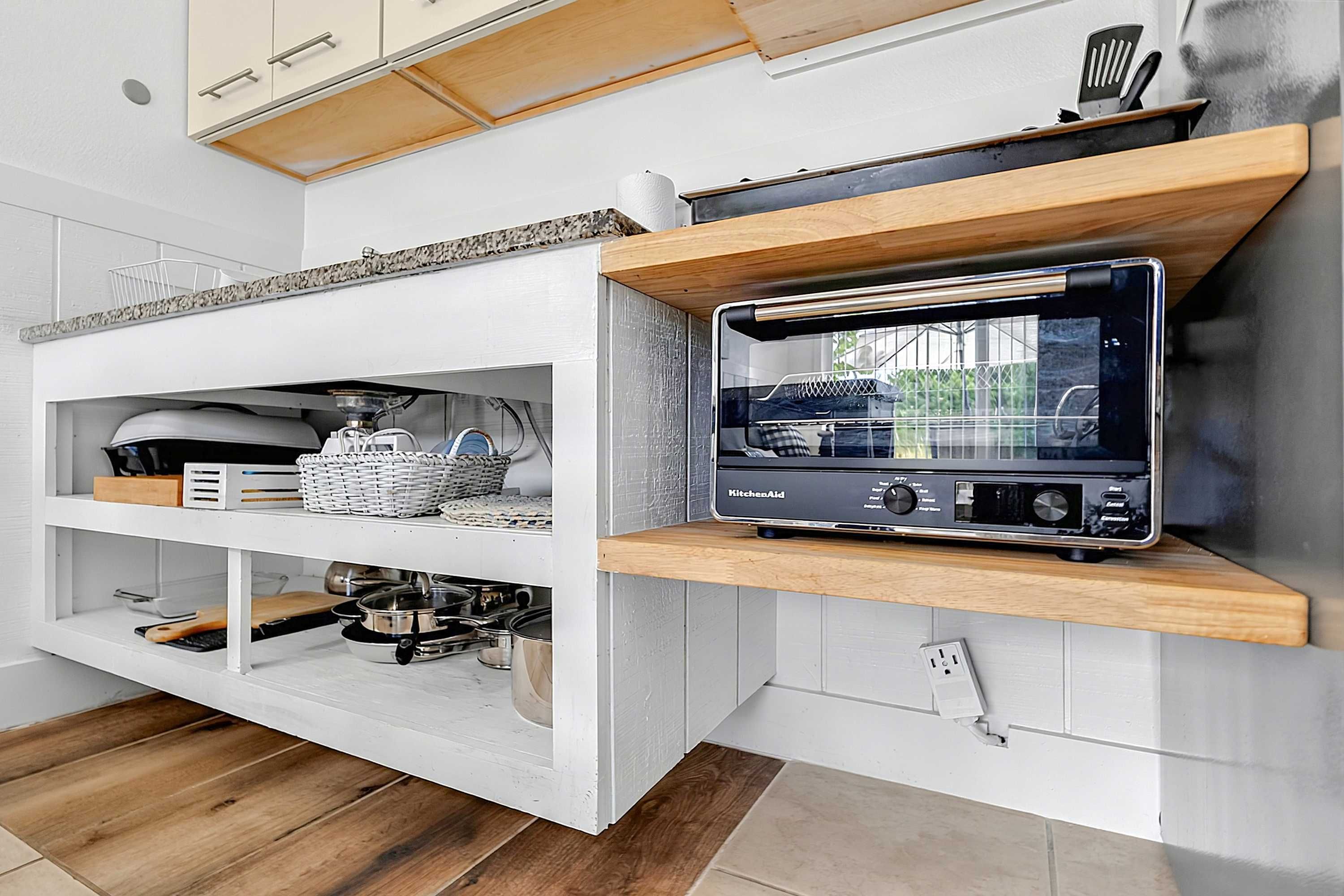 A kitchen with white cabinetry, wooden shelves, and a built-in radio.