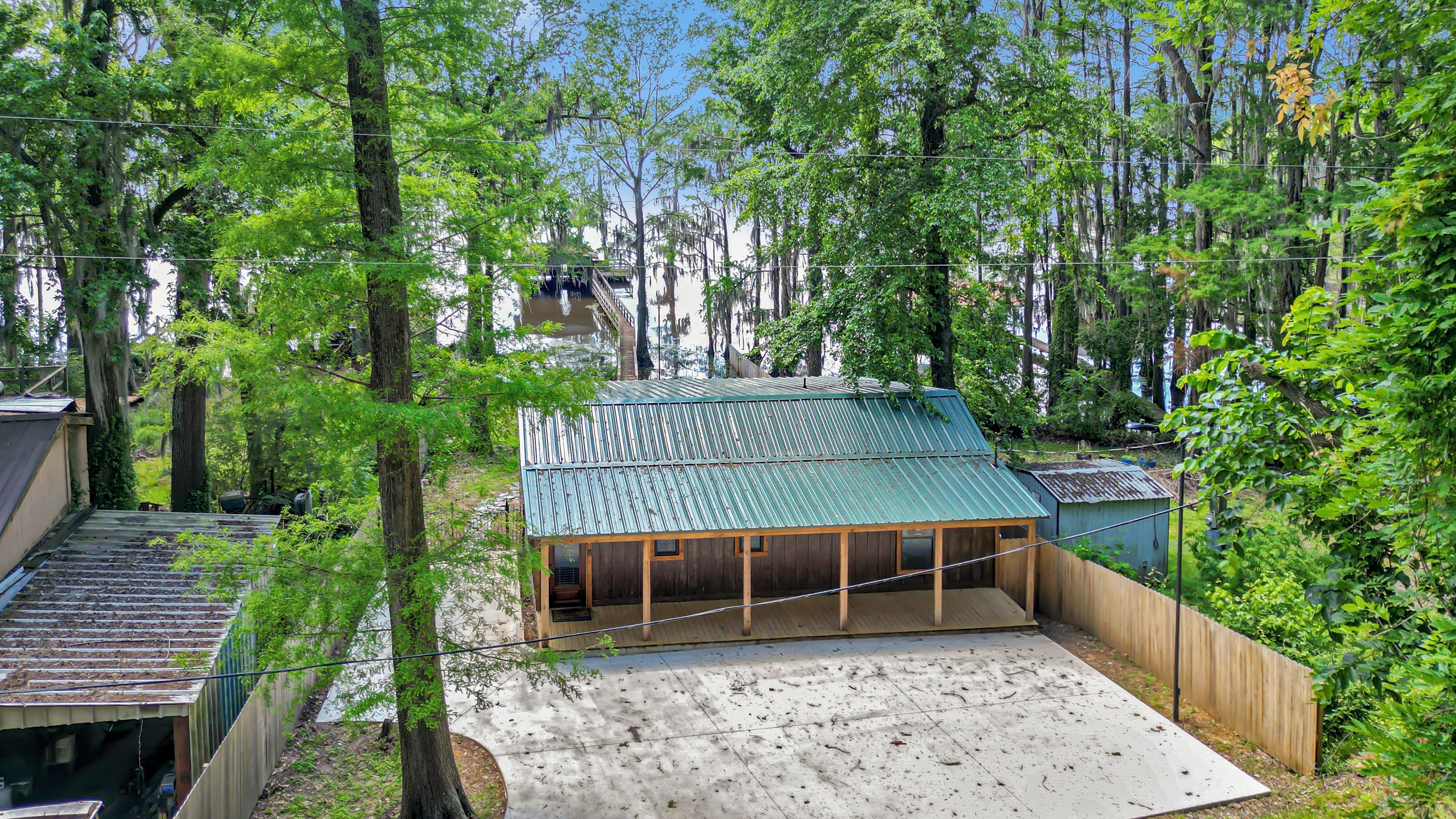 A covered outdoor area with a concrete floor, surrounded by trees and a wooden fence.