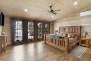 Une chambre avec un lit en bois, un ventilateur de plafond et de grandes fenêtres équipées de stores.
