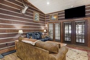 A log cabin interior with a leather sofa, a mounted deer head, and a television.