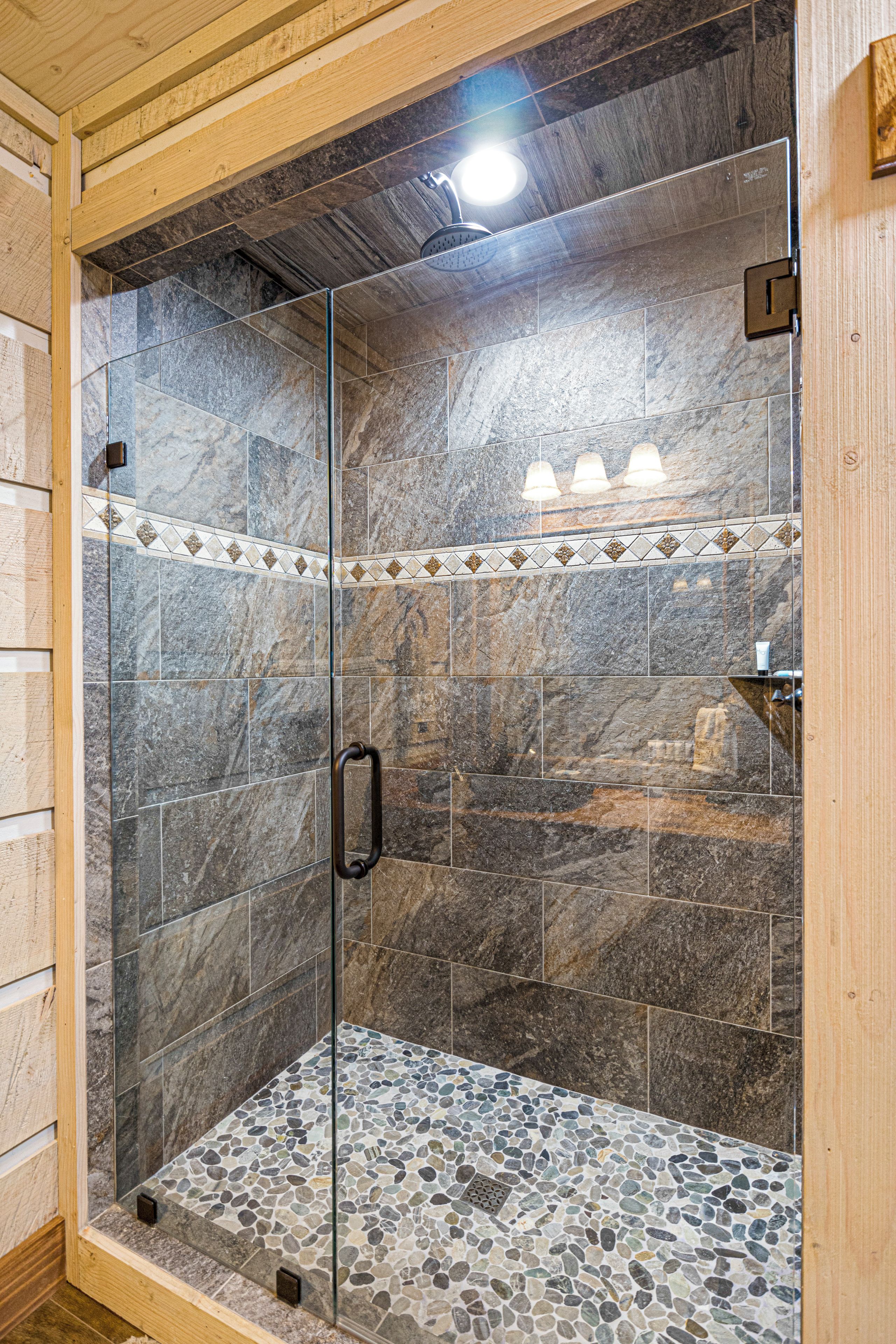 A glass-enclosed shower with stone tiles and a pebble-patterned floor.