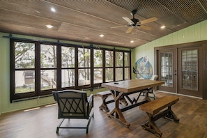 A dining area with a wooden table and benches, large windows with views of trees, and a ceiling fan.