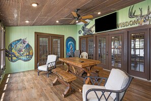 Un comedor con mesa de madera y bancos, ventilador de techo y obras de arte en las paredes.