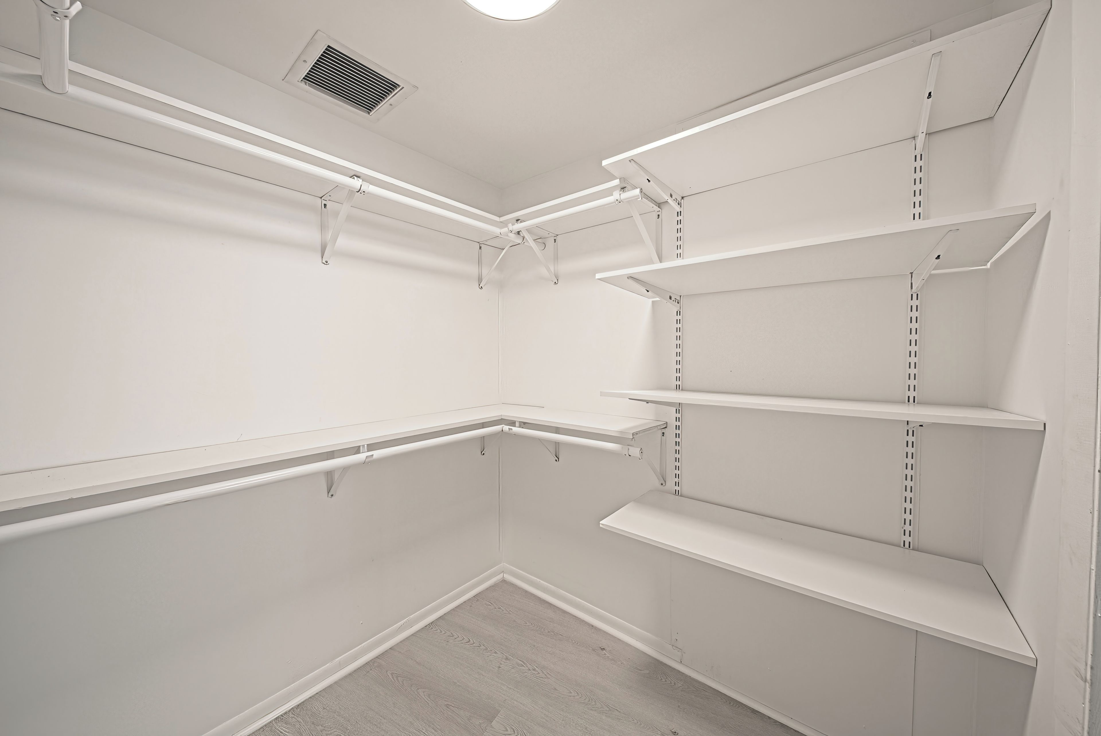 A white closet with multiple shelves and a vent on the ceiling.