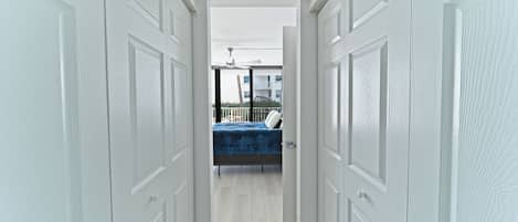 A hallway with white doors leading to a balcony with a bed.