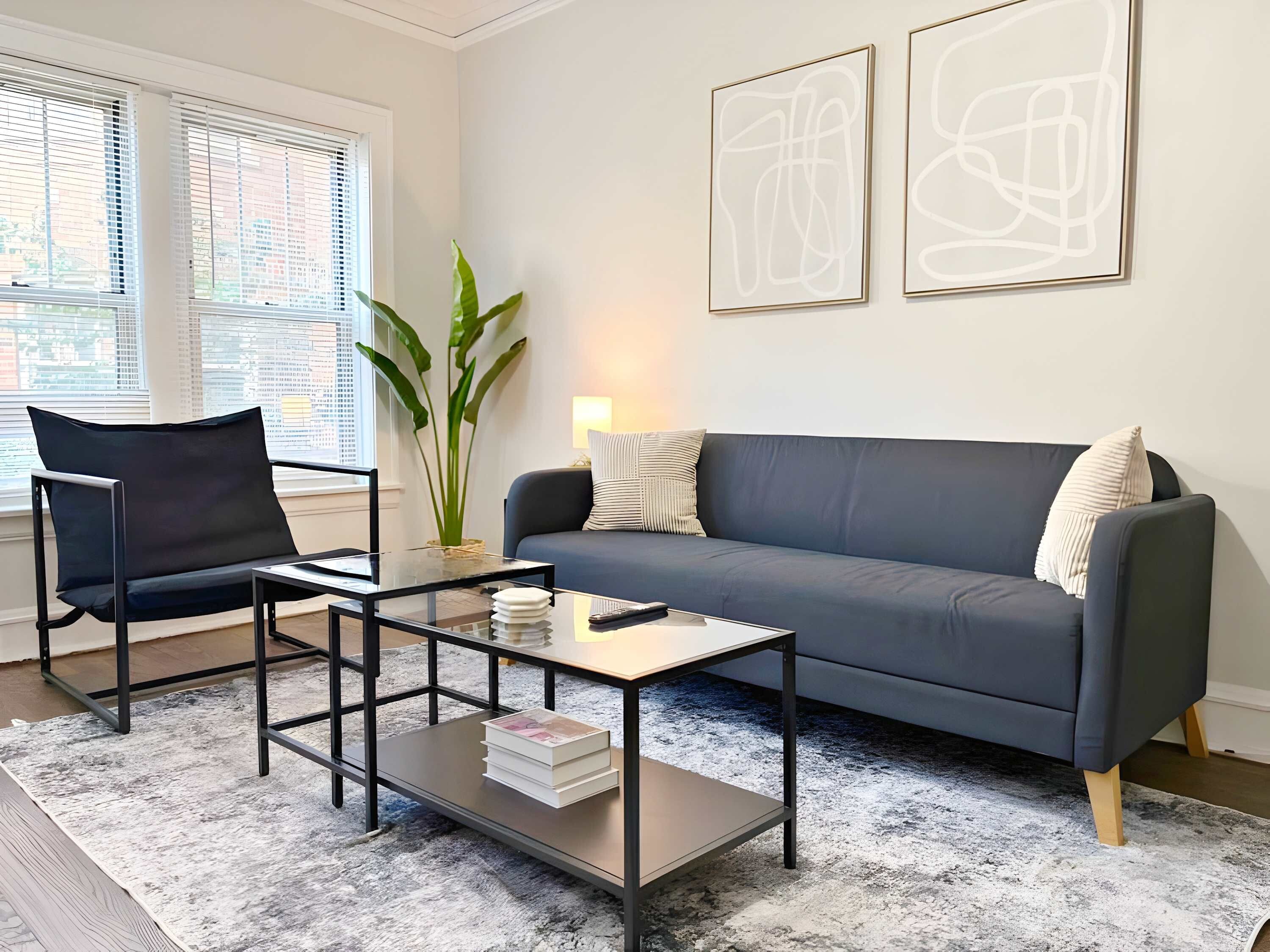 Ein modernes Wohnzimmer mit einem dunkelblauen Sofa, einem schwarzen Sessel, einem Glastisch und abstrakter Wandkunst.