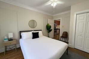 Een hotelkamer met een groot bed, een nachtkastje met lamp, een stoel, een spiegel en uitzicht op de keuken.