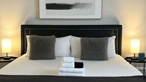 Una cama bien hecha con cabecera negra, dos almohadas mullidas y una pila de toallas.