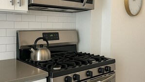 Una cocina con estufa, horno y microondas de acero inoxidable, y un reloj en la pared.
