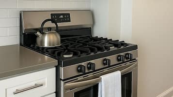 Una cocina con estufa, horno y microondas de acero inoxidable, y un reloj en la pared.
