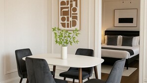 Un comedor con una mesa redonda, cuatro sillas, un florero con plantas verdes y una obra de arte abstracta colgada en la pared.
