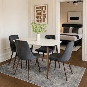 Uma sala de jantar com mesa redonda, quatro cadeiras, um vaso com plantas verdes e uma obra de arte abstrata na parede.