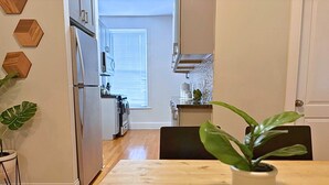 A dining area with a wooden table and chairs, a potted plant, and a kitchen in the background. - Beautifully Set Up 2BR Space (Chicago)