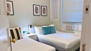 A hotel room with two beds, a nightstand with a lamp, a window with blinds, and artwork on the wall. - Beautifully Set Up 2BR Space (Chicago)