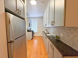 Cozinha estreita com piso de madeira, eletrodomésticos de aço inoxidável e armários em tons claros.