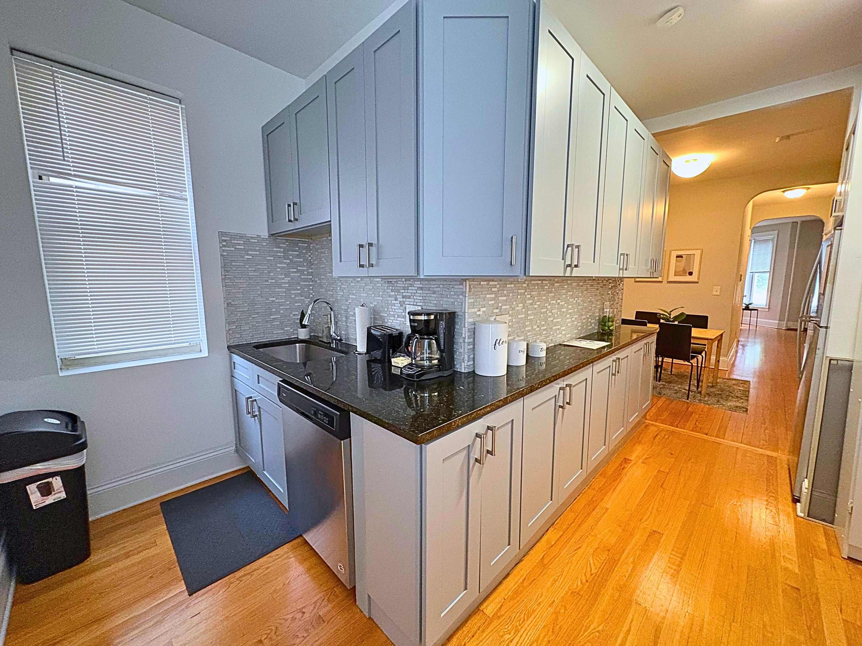 A modern kitchen with grey cabinets, a black countertop, and a dishwasher.