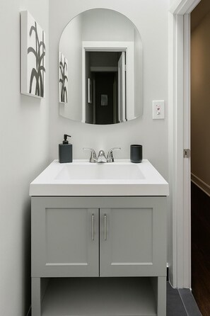 Un baño moderno con un tocador blanco, un espejo grande y un dispensador de jabón negro.