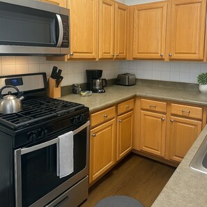 A kitchen with wooden cabinets, a stove, a microwave, a coffee maker, and a toaster. - 1BR Pad with Homey Feel (Chicago)