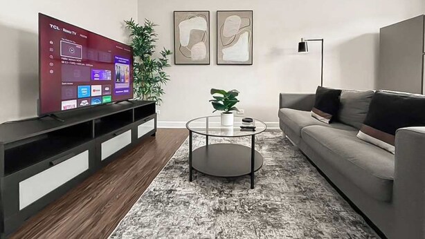 Ett vardagsrum med en platt-TV, en grå soffa, ett soffbord och två abstrakta tavlor på väggen.