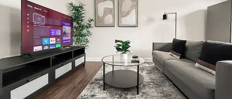 A living room with a flat-screen TV, a grey sofa, a coffee table, and two abstract paintings on the wall.