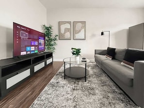 A living room with a flat-screen TV, a grey sofa, a coffee table, and two abstract paintings on the wall.