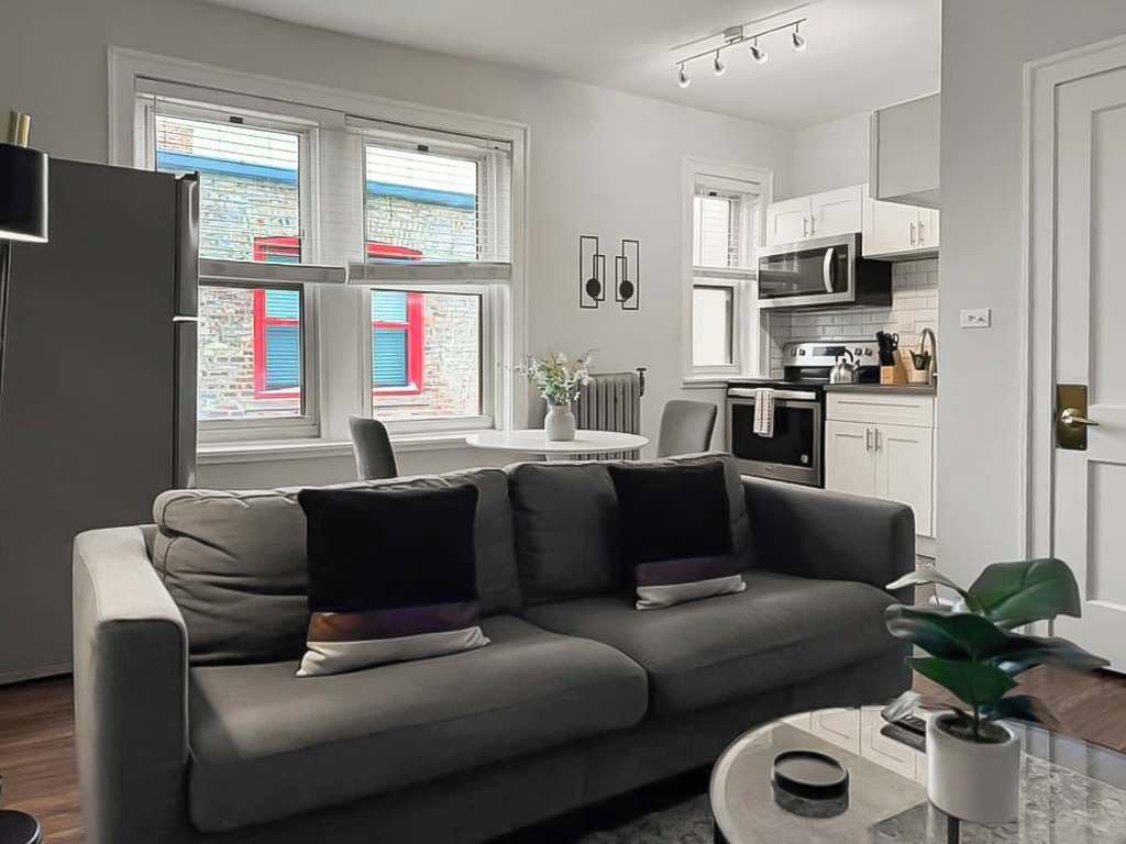 Un salón moderno con un sofá gris, una mesa de centro y vistas al exterior a través de amplios ventanales.