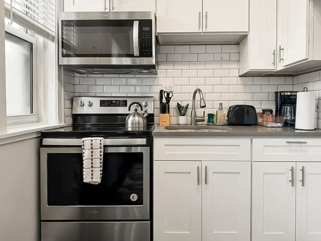 Una cocina moderna con electrodomésticos de acero inoxidable, armarios blancos y salpicadero de azulejos.