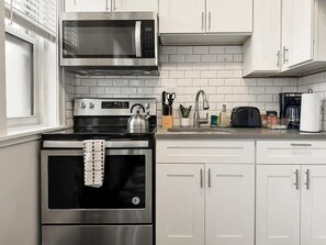 A modern kitchen with stainless steel appliances, white cabinetry, and a tiled backsplash.