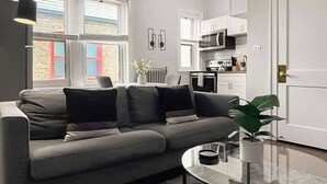 Ett modernt vardagsrum med en grå soffa, ett soffbord i glas och en krukväxt.