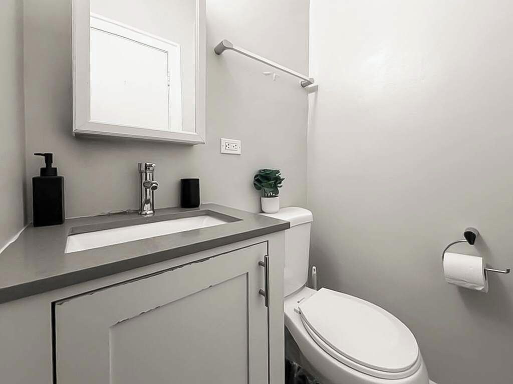 Un baño con inodoro blanco, lavamanos con grifo, dispensador de jabón y soporte para papel higiénico.