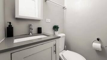 Un baño con inodoro blanco, lavamanos con grifo, dispensador de jabón y soporte para papel higiénico.