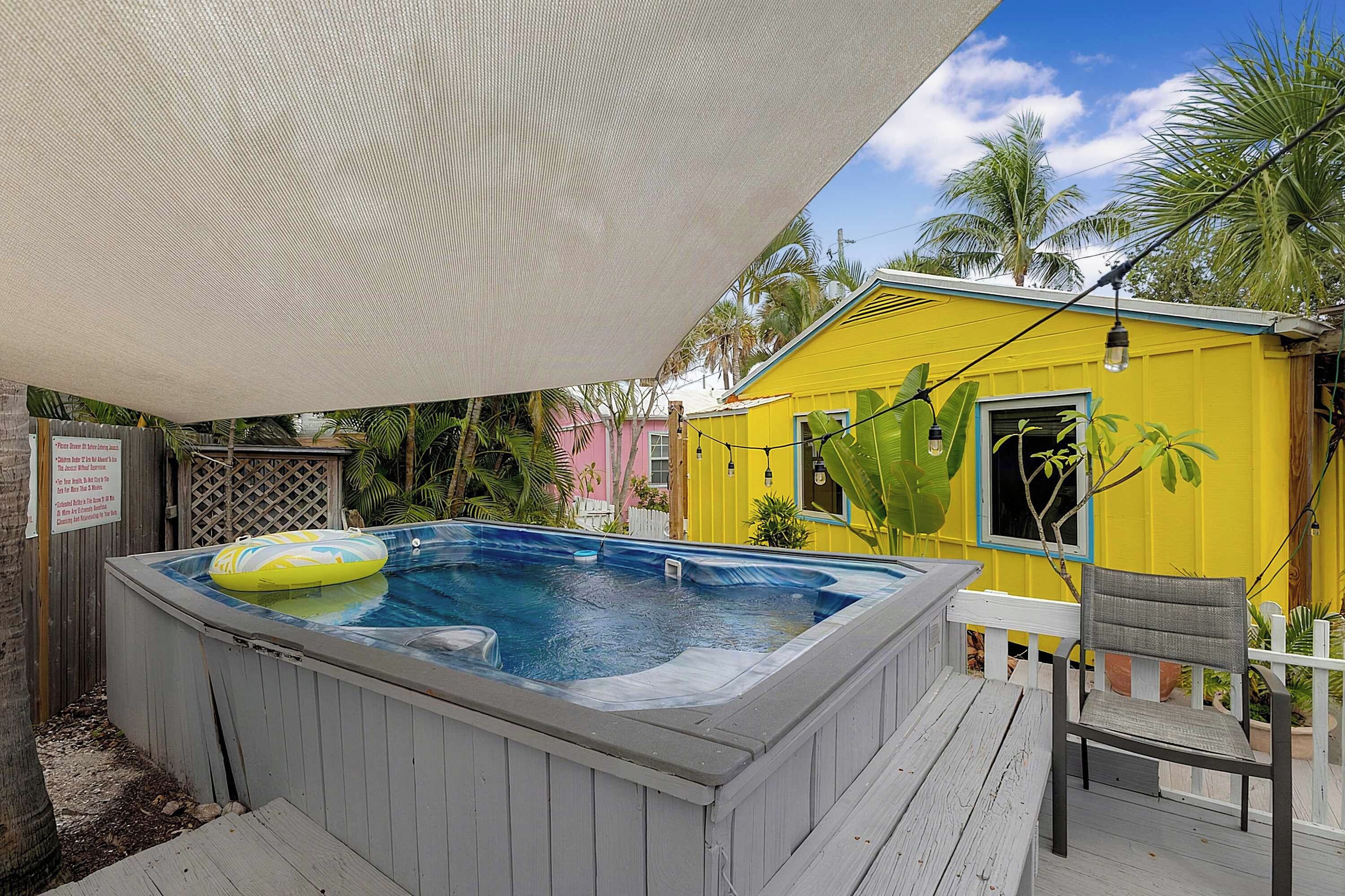 Ein Whirlpool mit Schwimmbad, ein gelbes Gebäude und eine Holzterrasse mit einem Stuhl.