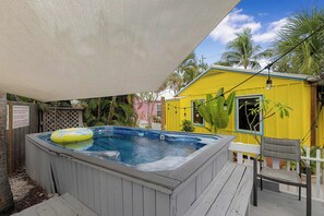 Ein Whirlpool mit Schwimmbad, ein gelbes Gebäude und eine Holzterrasse mit einem Stuhl.