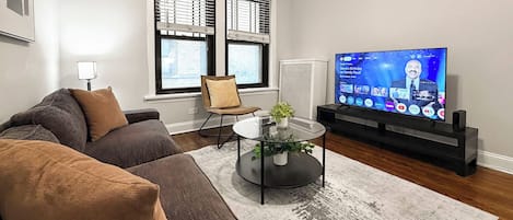 A modern living room with a sectional sofa, a glass coffee table, and a flat-screen TV.