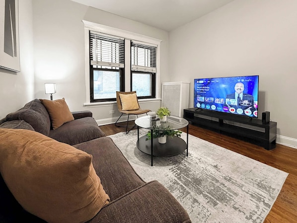 Een moderne woonkamer met een hoekbank, een glazen salontafel en een flatscreen televisie.