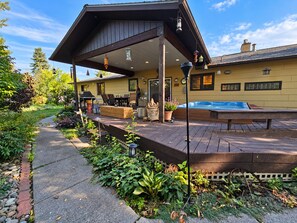 A covered outdoor deck with a hot tub, a barbecue grill, and a seating area.