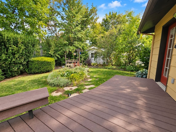 A wooden deck with a bench, surrounded by a well-maintained garden with various plants and a small pond.