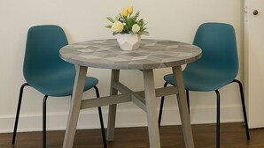 A round table with a geometric tile top, flanked by two teal chairs, a white vase with yellow flowers, and a black and white abstract painting on the wall. - Trendy Studio Apartment in Chicago (Chicago)