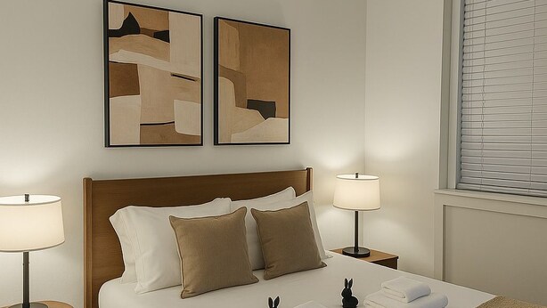 A neatly made bed with pillows, a bedside lamp, and a small table with a lamp. There are two abstract paintings on the wall above the bed. - Trendy Studio Apartment in Chicago (Chicago)