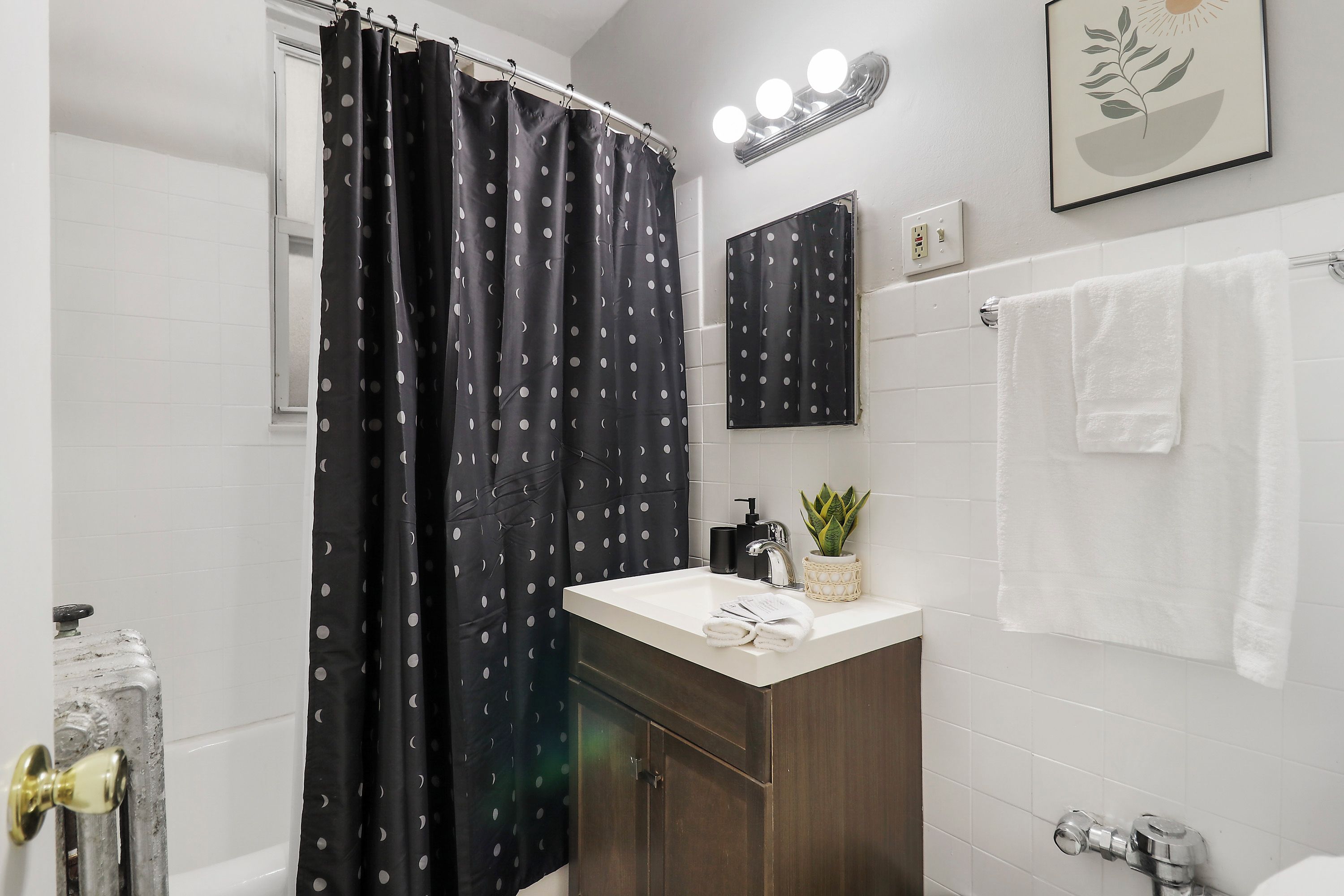 Un baño con cortina de ducha, lavamanos, espejo, toallero y una planta en maceta.