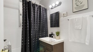 A bathroom with a shower curtain, a sink, a mirror, a towel rack, and a potted plant. - Trendy Studio Apartment in Chicago (Chicago)