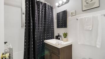 Un baño con cortina de ducha, lavamanos, espejo, toallero y una planta en maceta.