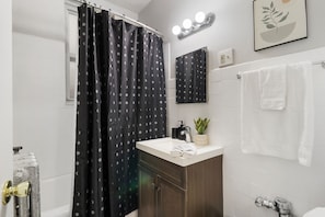 Een badkamer met douchegordijn, wastafel, spiegel, handdoekhouder en een kamerplant.